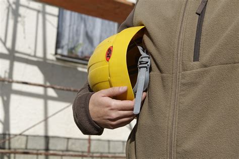 Osoba s prilbou a reflexnou vestou kontroluje stavebný plán na stavenisku